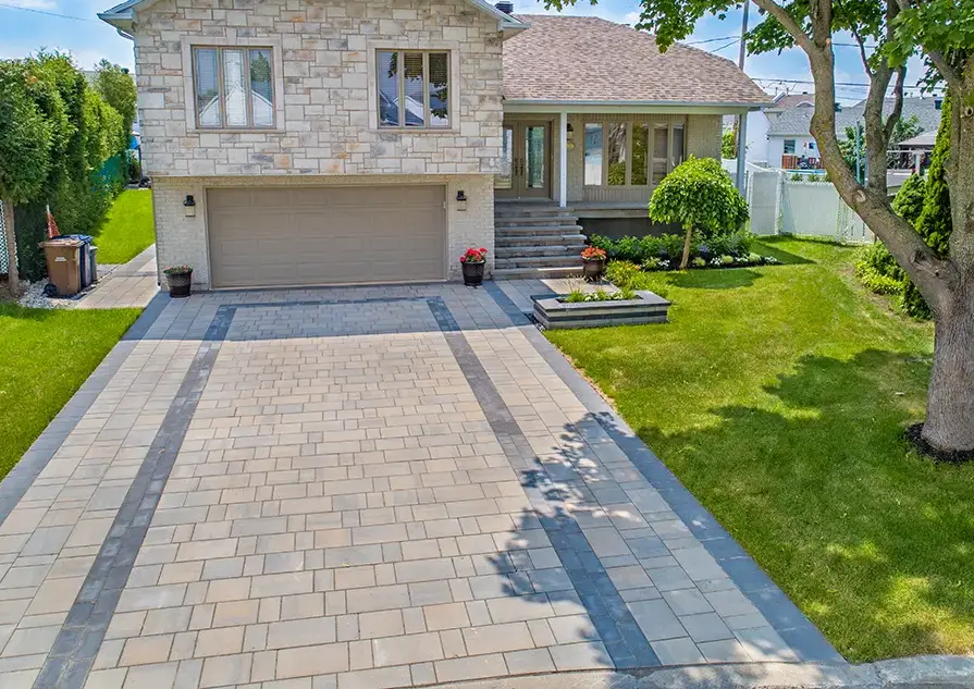 Aménagement paysager moderne d'une entrée de maison sur la Rive-Sud de Montréal avec pavé uni beige et gris, plates-bandes fleuries et muret décoratif devant un garage.