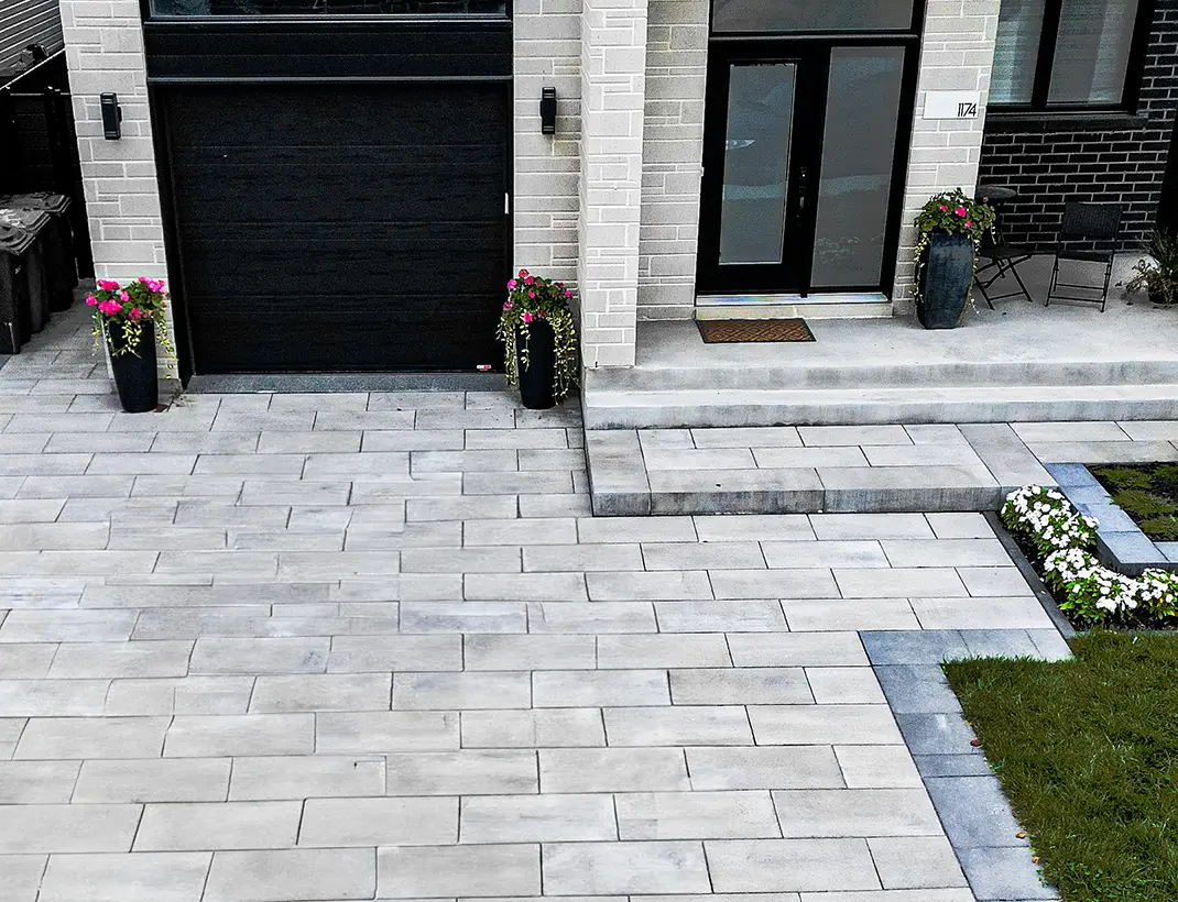 Entrée de garage et trottoir de façade en pavé uni gris contemporain pour une maison moderne à Montréal, incluant des jardinières décoratives.